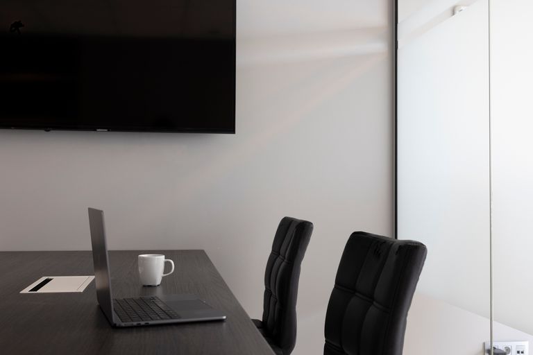 A sleek, modern office setup with a laptop, cup, and TV in an empty conference room.